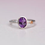 Front view of a sterling silver ring with a bezel-set oval amethyst and a small orange sapphire accent in a 14k gold bezel on the band