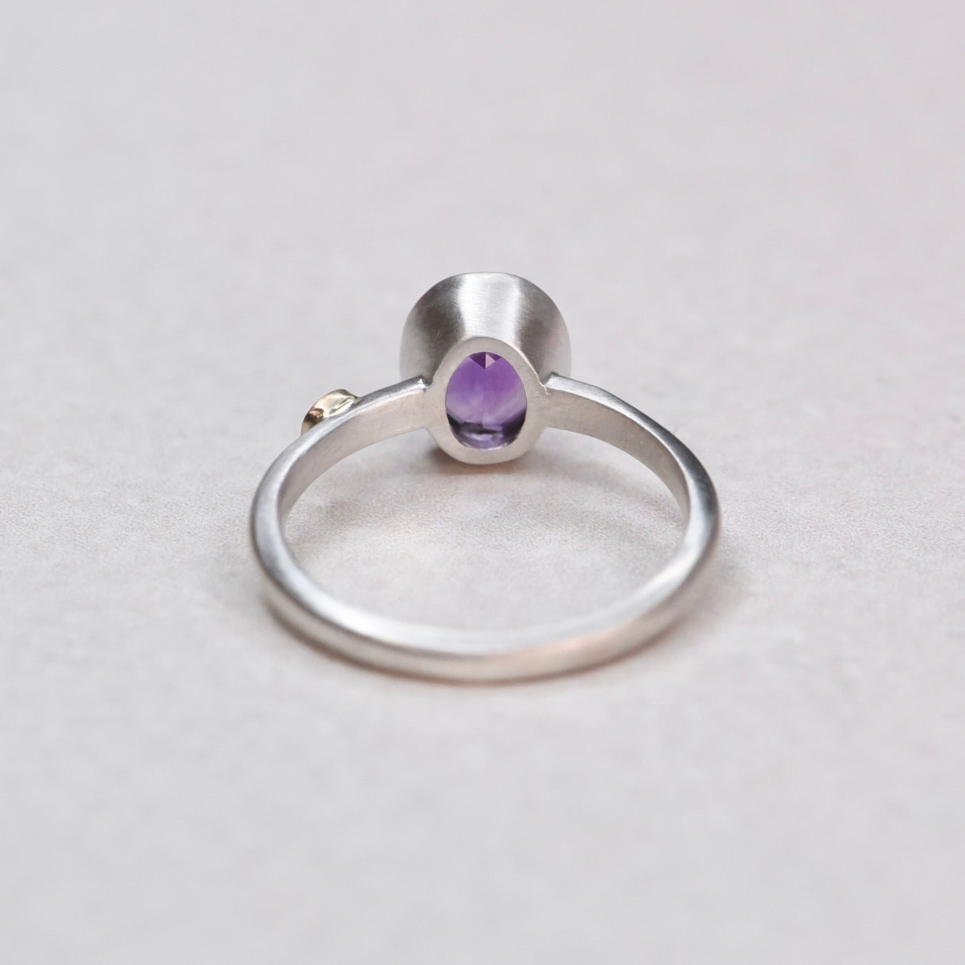 Back view of a sterling silver bezel-set oval amethyst ring showing the band and setting construction