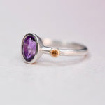 Side angle view of a sterling silver ring showing the oval amethyst bezel and orange sapphire set in 14k gold on the band