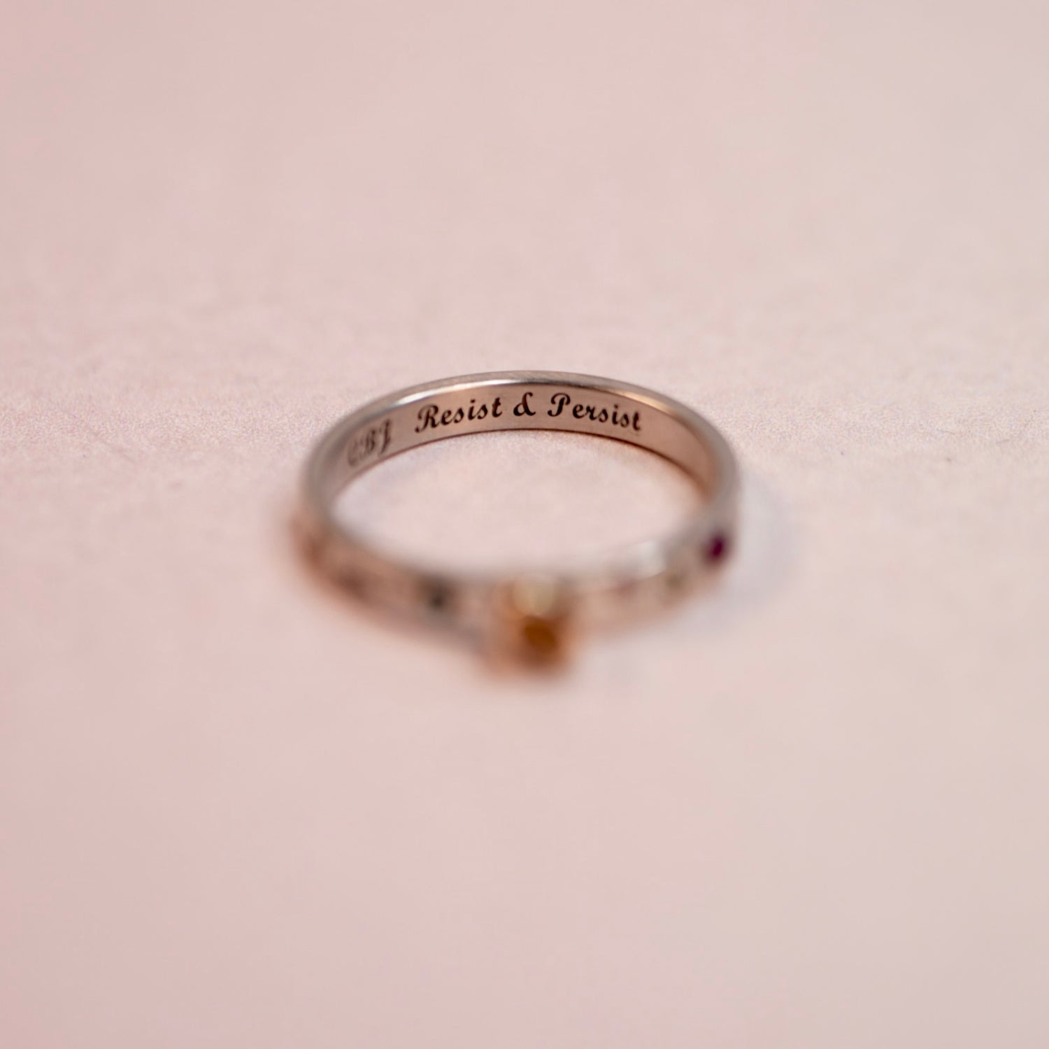 Silver ring with 'Resist & Persist' engraving on a beige background