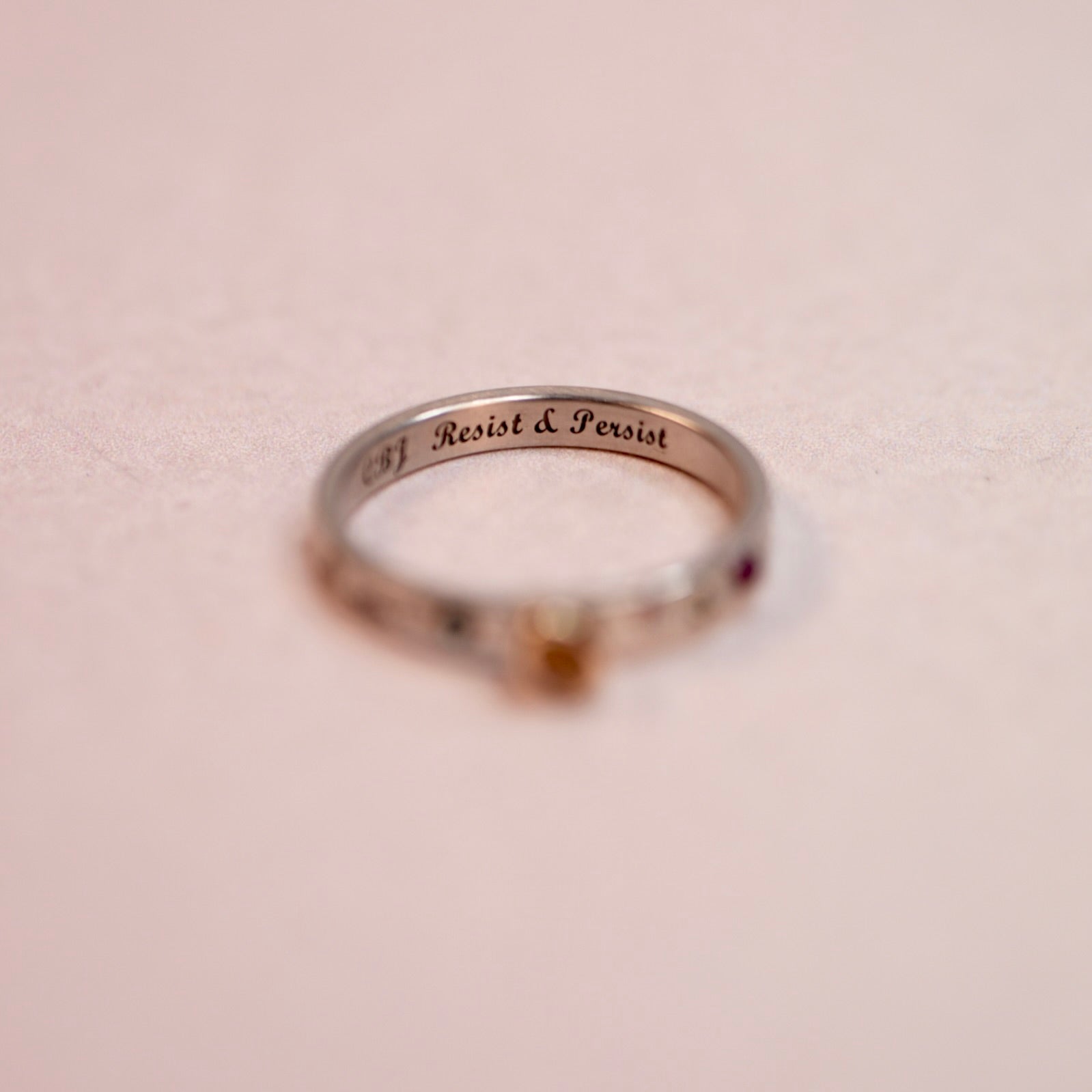 Silver ring with 'Resist & Persist' engraving on a beige background