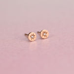 Close-up of Celestial Diamond Studs on a White Background – A pair of small, delicate diamond studs set in gold with a starburst design. Each stud features a sparkling round diamond in the center, surrounded by fine, textured details that give a celestial look.