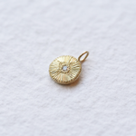 Flat lay of the Reborn 18k Gold Charm on a soft linen surface, paired with other gold jewelry for a styled presentation