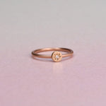 A delicate rose gold ring with a small star-shaped diamond set on a 14k yellow disc with a white diamond. on a pionk background