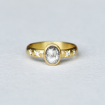An 18k yellow gold ring with a central oval salt and pepper diamond, accompanied by smaller accent diamonds set in a hand-engraved design.