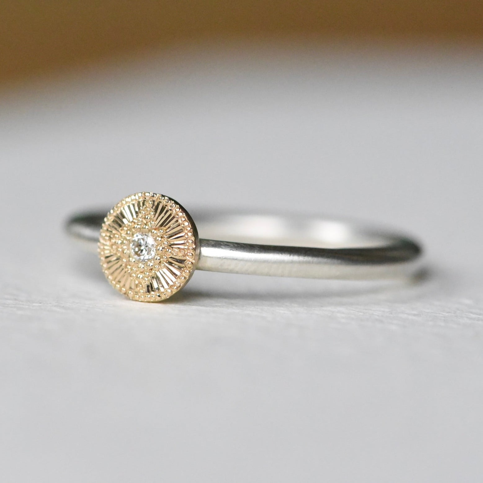Gold and silver ring with a diamond on a light gray background