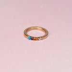 Top view of one of a kind 10k yellow gold ring with Sleeping Beauty turquoise blue sapphire orange sapphire and diamonds on pink background