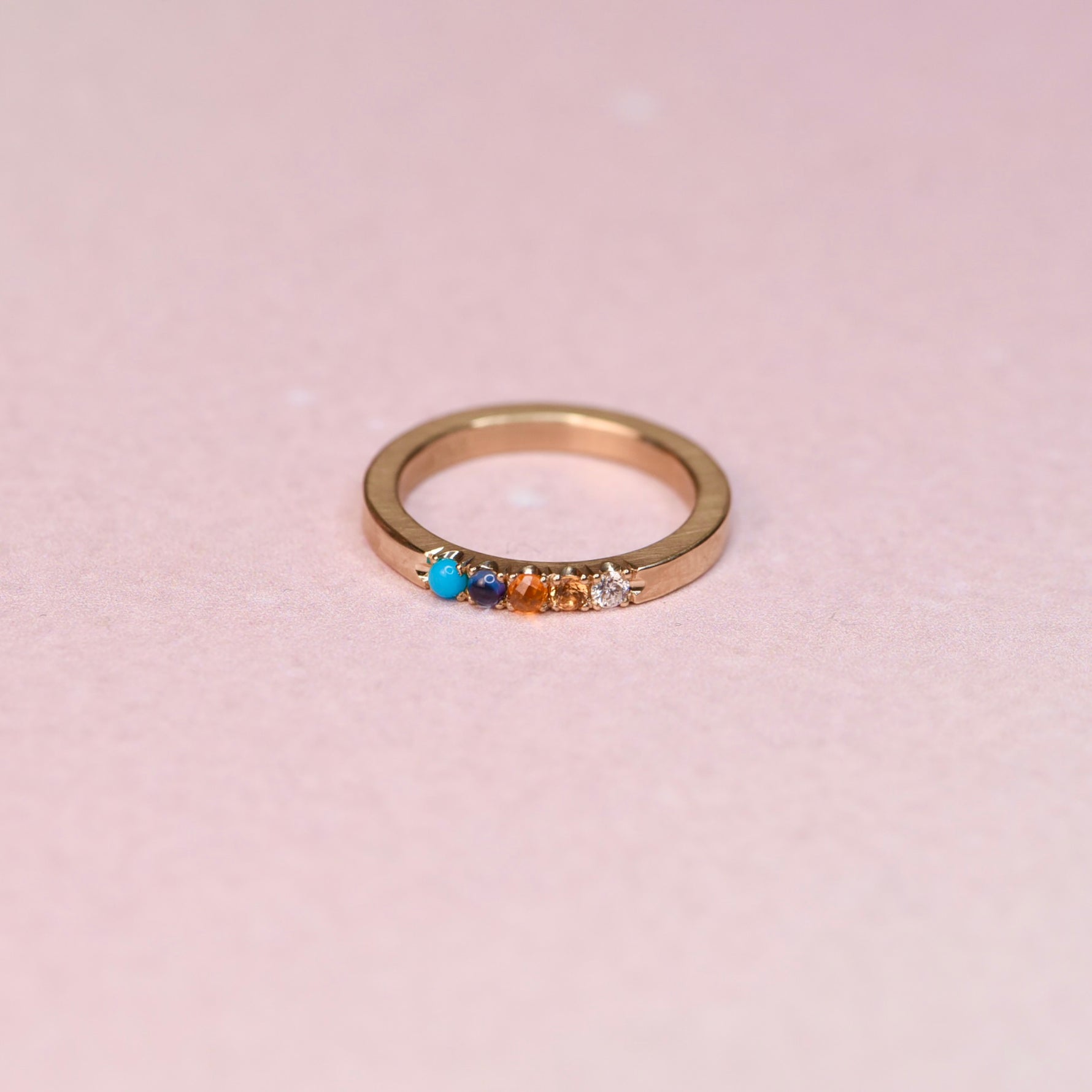 Top view of one of a kind 10k yellow gold ring with Sleeping Beauty turquoise blue sapphire orange sapphire and diamonds on pink background