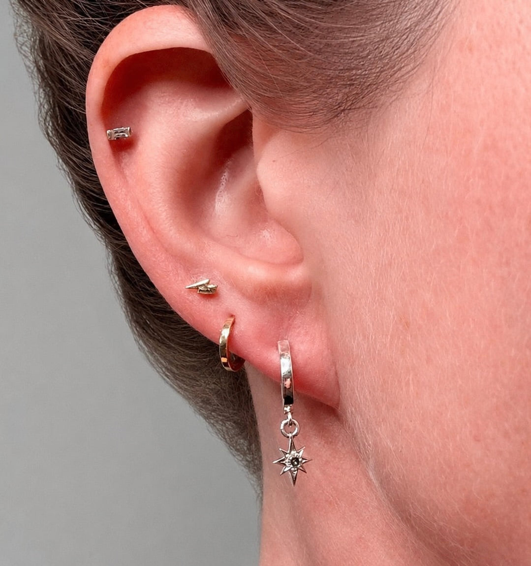 Sterling silver star dangle huggie hoop earring with blue sapphire worn on a model's ear