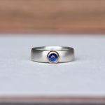 Strength Sapphire Mixed Ring on a white background, featuring a deep blue sapphire set in a 14k gold bezel with a satin finish sterling silver band. Created by Corkie Bolton.