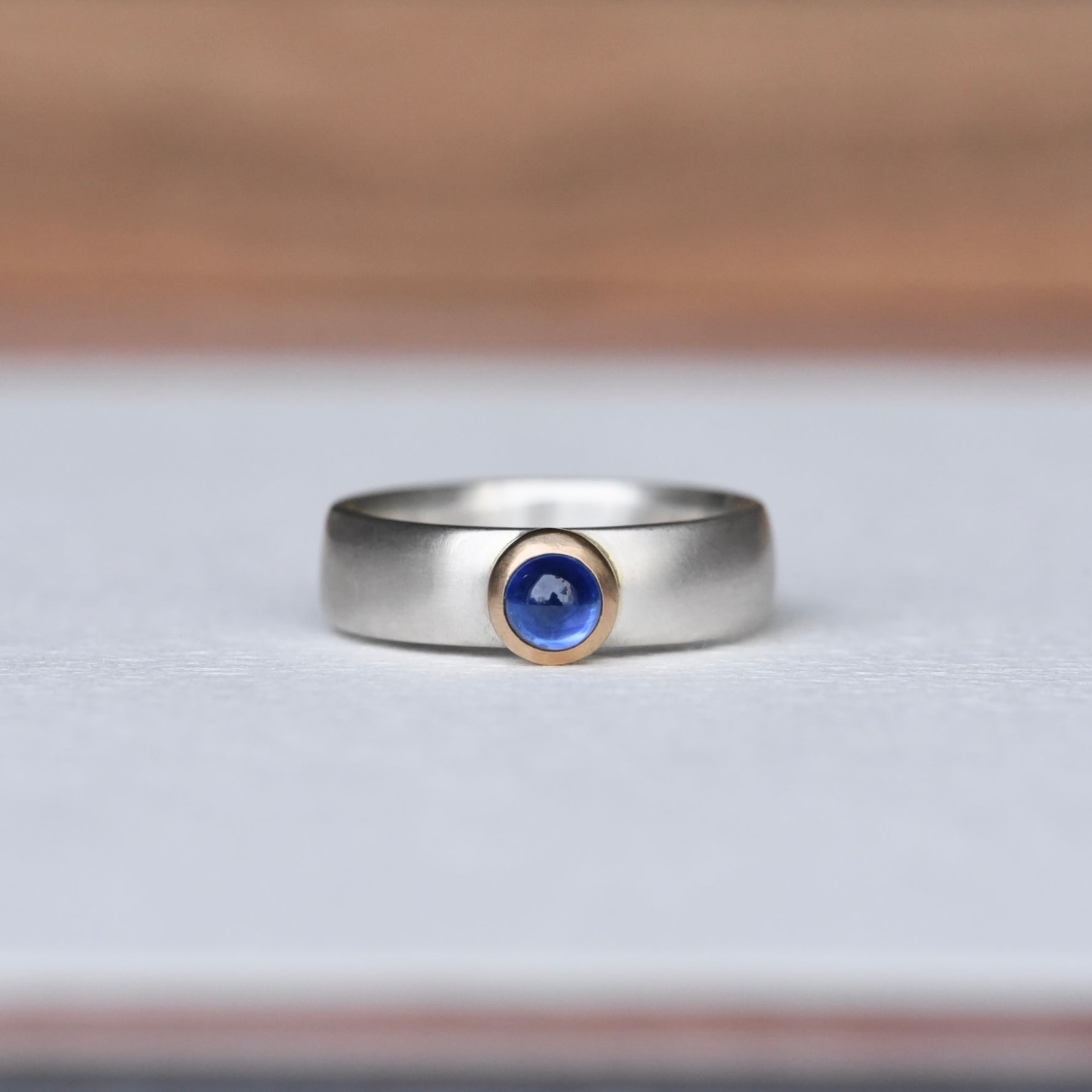 Strength Sapphire Mixed Ring on a white background, featuring a deep blue sapphire set in a 14k gold bezel with a satin finish sterling silver band. Created by Corkie Bolton.