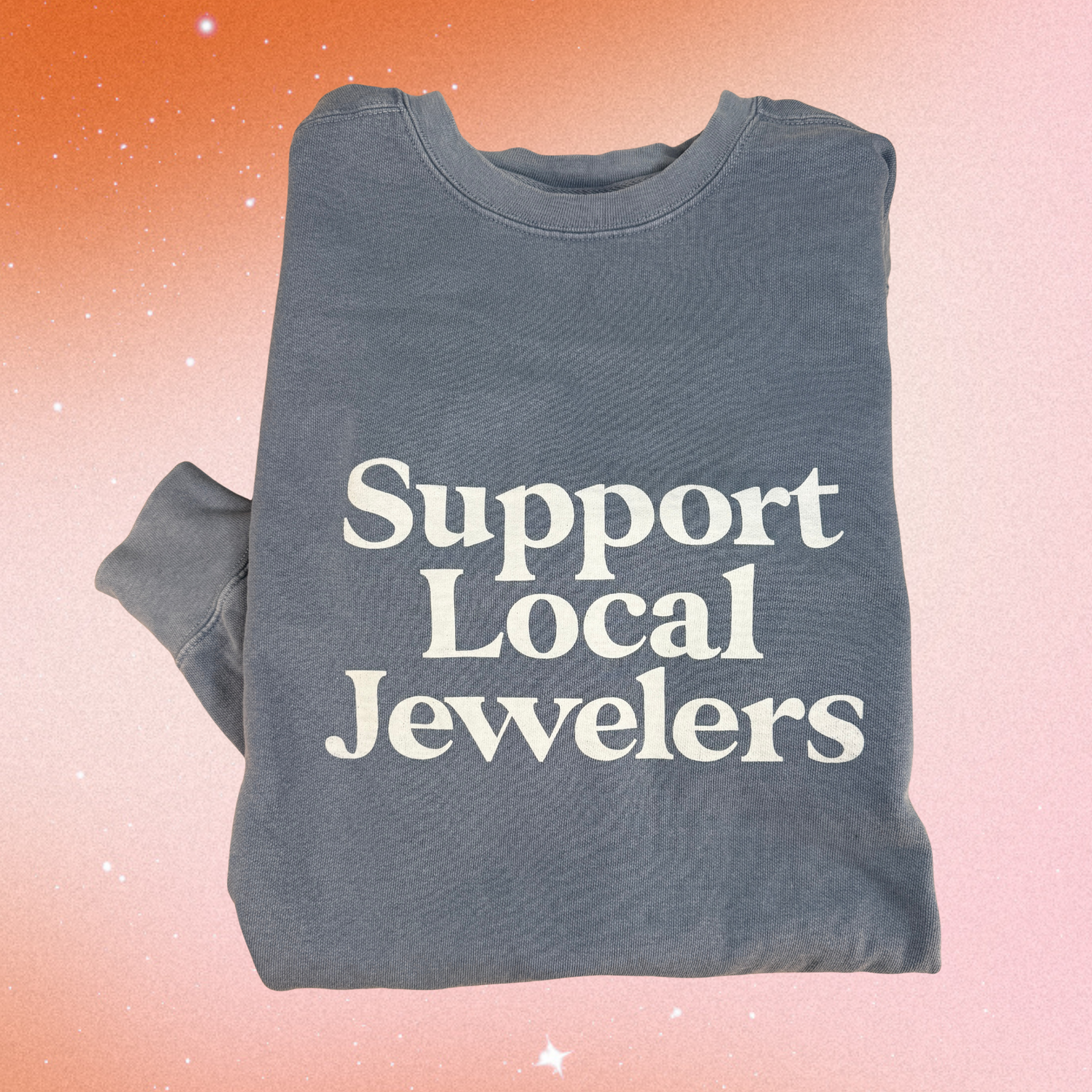 Folded blue denim sweatshirt with 'Support Local Jewelers' text. Photographed on a gradient background