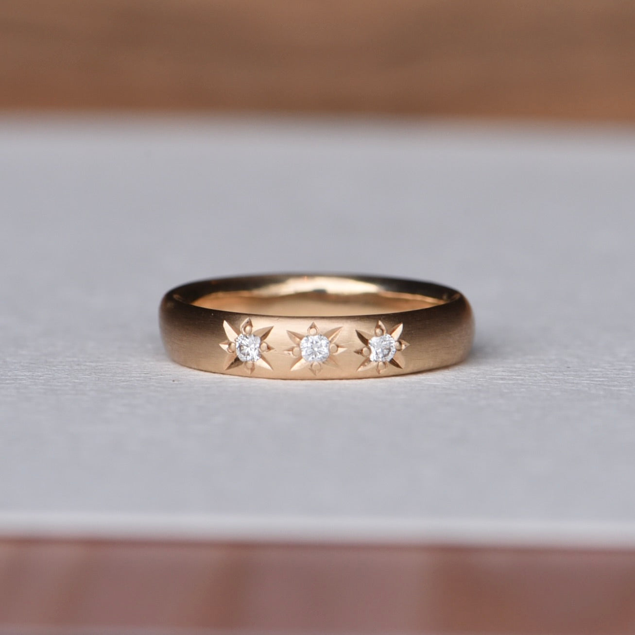 Trio Diamond Band - Size 6.5. A polished gold band featuring three diamonds set in engraved star settings, evoking a vintage-inspired elegance. The star-set diamonds offer a classic touch with intricate detailing and brilliant sparkle.
