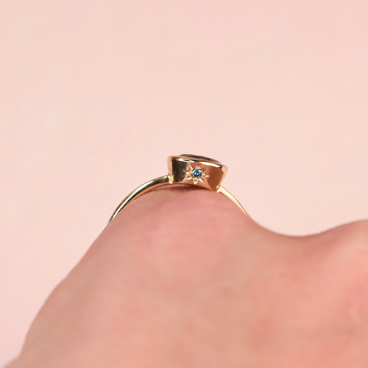 Side view of a gold ring worn on a finger, showing the teal diamond in a hand engraved star setting on the bezel