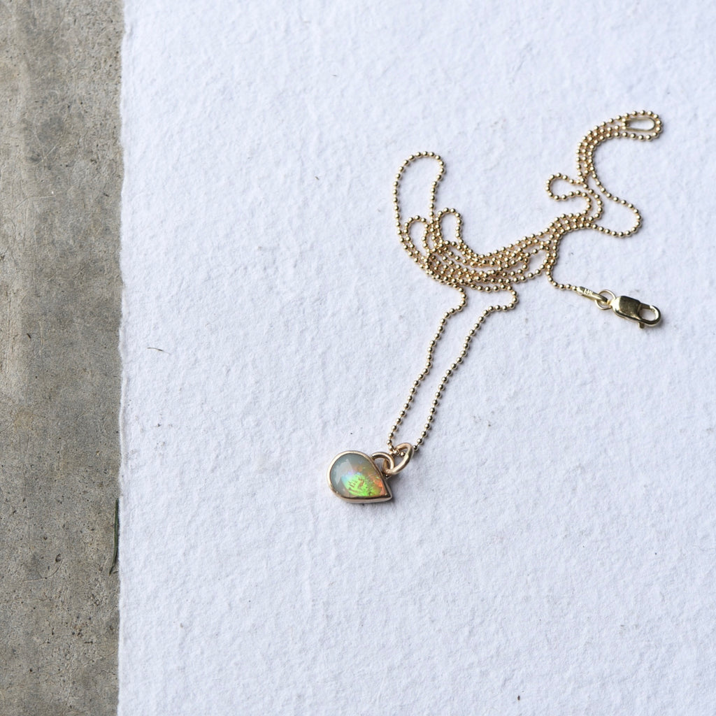 A teardrop flashy opal set in 14k gold as a charm, created by Corkie Bolton Jewelry.