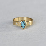 Gold ring with hand engraved star settings and diamonds and a teardrop shaped turquoise cabochon with black matrix set in a thick gold bezel.