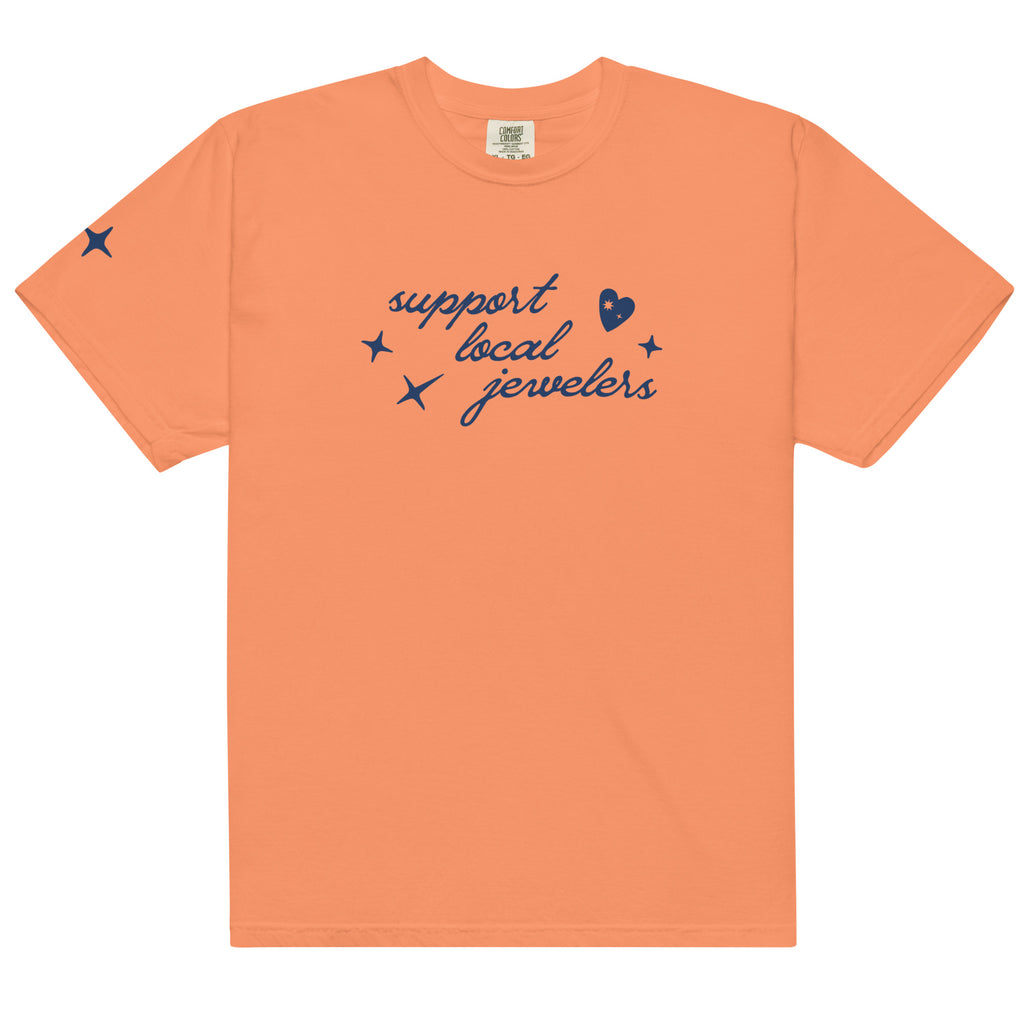 Light orange (Terracotta), short-sleeve T-shirt with a navy blue design on the front. The design includes the phrase "support local jewelers" in cursive font, accompanied by small star-like shapes and a heart with a sparkle inside. A small star detail is featured on the left sleeve.