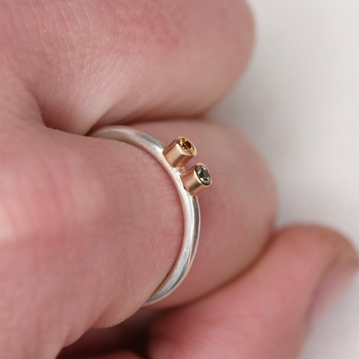 Close-up of a sterling silver stacker ring held in hand, showing two tiny sapphires in 14k gold bezels from the side