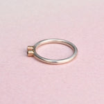 Side view of a slim sterling silver stacker ring with two 14k gold bezels on a pink background