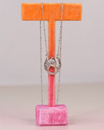 A sterling necklace with a horse ina horseshoe charm displayed on a pink velvet T-stand with an orange top bar against a light gray background.
