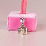 A sterling silver jewelry box pendant with a pink sapphire accent on the bail, displayed in front of a pink velvet jewelry stand.