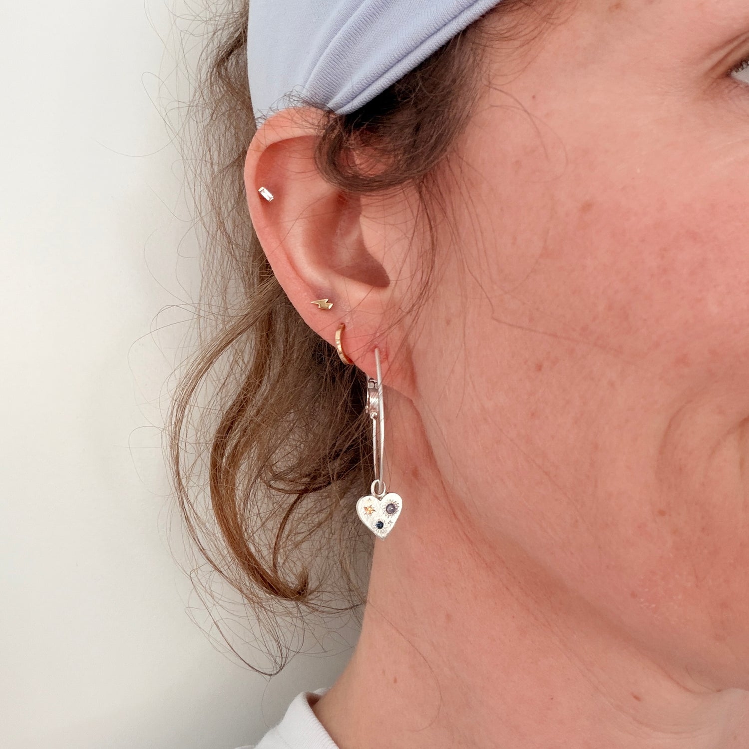 Close-up of a person wearing heart-shaped earrings with a plain background