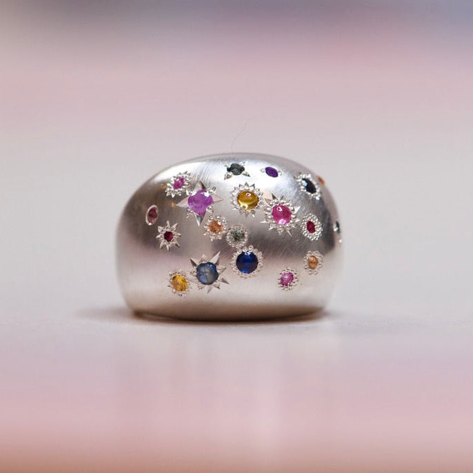 Silver ring with colorful gemstones on a blurred background