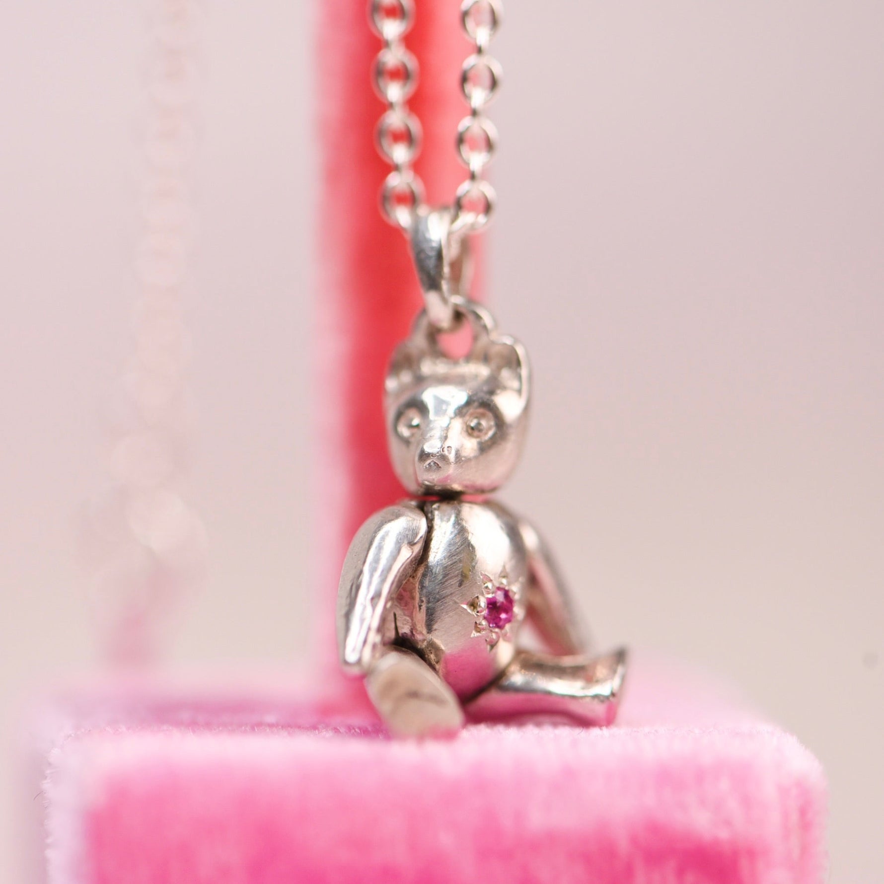 Vintage sterling silver articulating teddy bear charm necklace sitting on a pink velvet display, featuring a hand engraved star-set pink sapphire belly charm