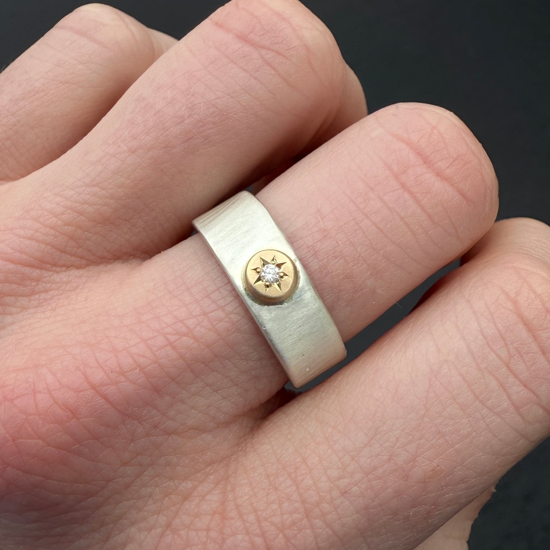(IMAGE 2) The Waves Engraved 14k Silver Diamond Ring in size 8.5 worn on a hand, showcasing its textured wave-like band, 14k gold star setting, and sparkling diamond against natural skin tone.
