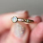 Angled view showing the bezel-set black opal from Lightning Ridge and hand-engraved star settings with pink sapphire, red sapphire, and diamond on the 14k yellow gold band. Being held by a hand with glitter nail polish.
