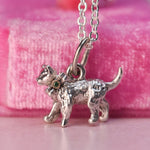 Close up of a vintage Beaucraft sterling silver kitten charm featuring a green diamond set in a 14k yellow gold bow. with a pink velvet background.