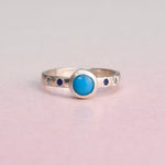 Front view of a handcrafted sterling silver ring featuring a bezel-set Sleeping Beauty turquoise with engraved star-set blue sapphires by Corkie Bolton Jewelry.