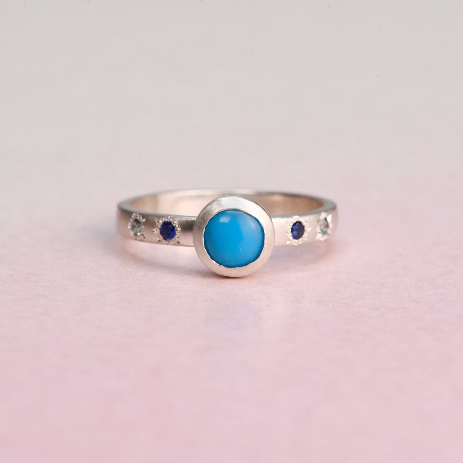 Front view of a handcrafted sterling silver ring featuring a bezel-set Sleeping Beauty turquoise with engraved star-set blue sapphires by Corkie Bolton Jewelry.