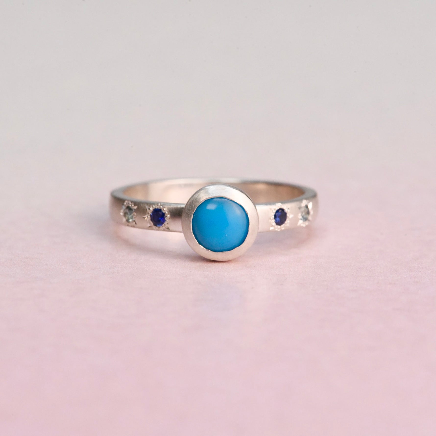 Front view of a handcrafted sterling silver ring featuring a bezel-set Sleeping Beauty turquoise with engraved star-set blue sapphires by Corkie Bolton Jewelry.