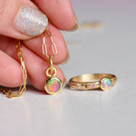Gold necklace and ring with opal stones held by a hand with glittery nail polish.