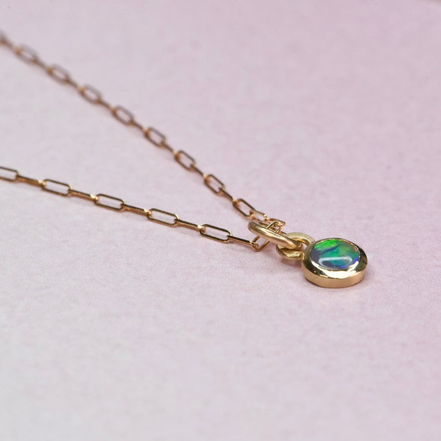 Gold necklace with an opal pendant on a light pink background