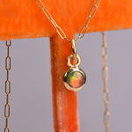 18k yellow gold necklace featuring a one-of-a-kind ethically sourced black Australian opal by Ancients17 with bold neon flashes of red, orange, blue, and green, hand engraved peace sign on the back by Corkie Bolton Jewelry