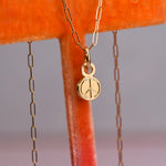 Gold necklace with a hand engraved peace symbol pendant on an orange velvet surface.