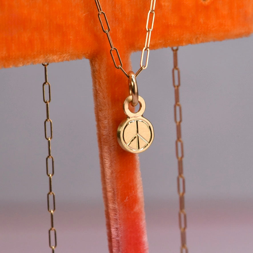Gold necklace with a hand engraved peace symbol pendant on an orange velvet surface.