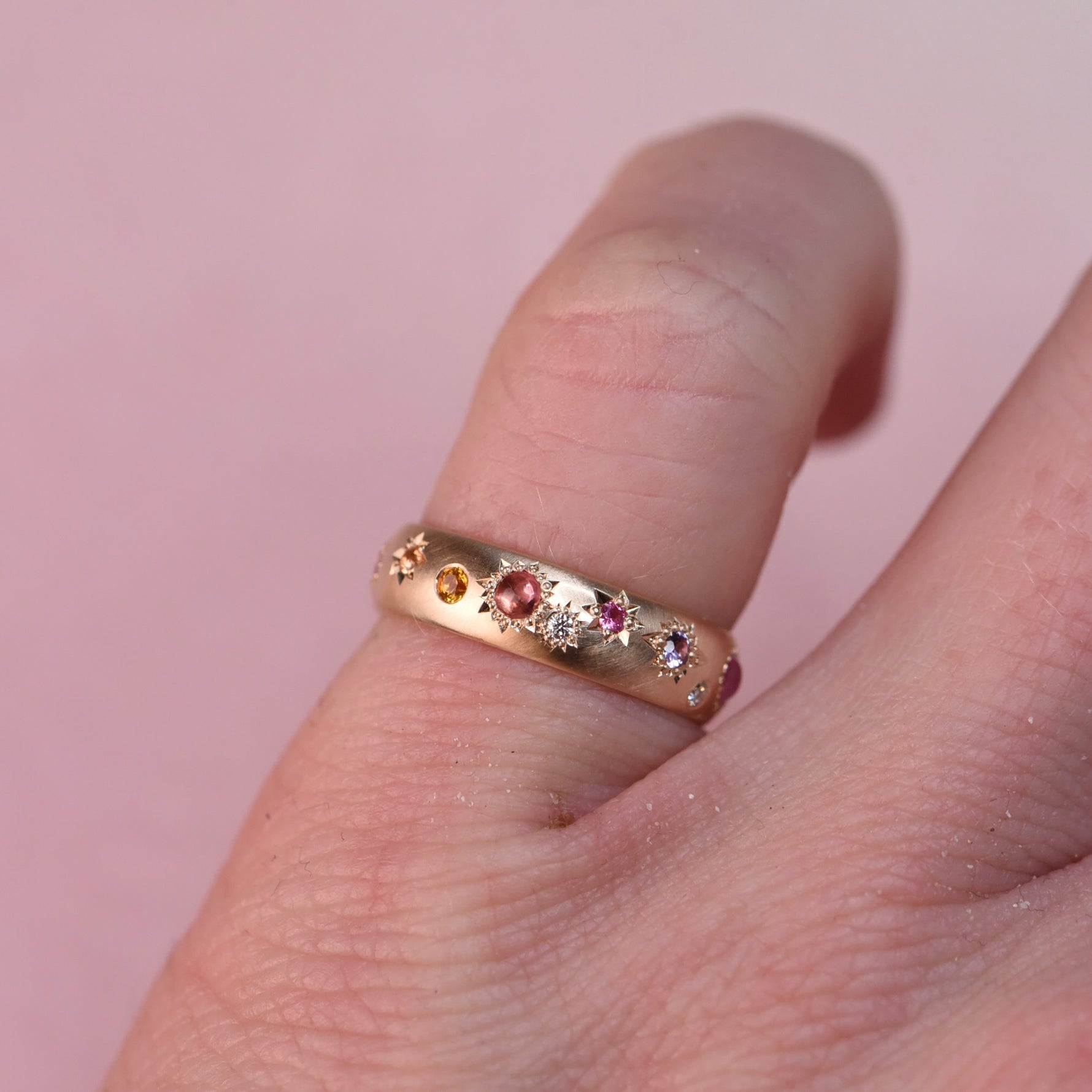 Vintage Confetti Diamond + Sapphire Band worn on a pinky finger, showing the multicolor stones and star-engraved details in soft natural light.
