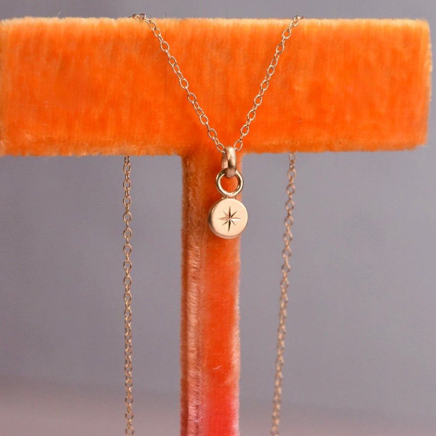 Gold necklace with a star pendant on an orange stand against a gray background