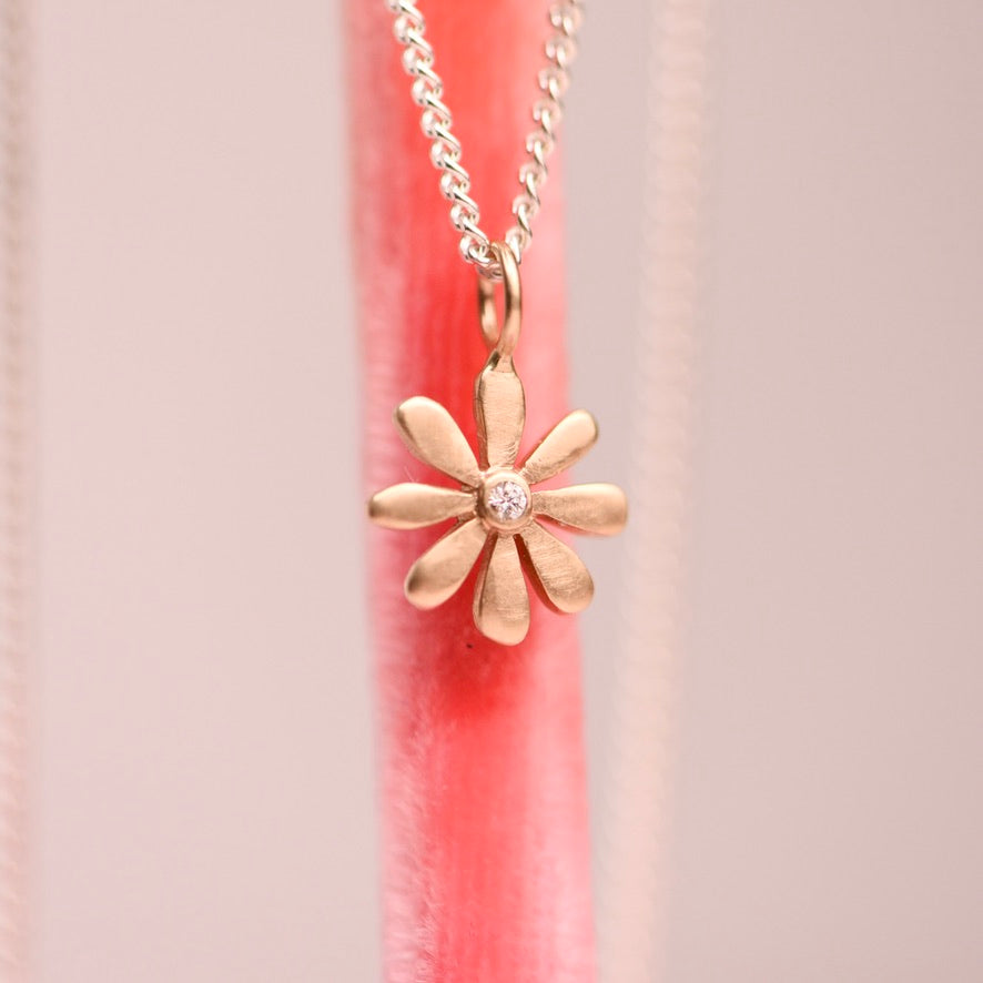 Gold flower-shaped pendant on a chain against a pink and beige background