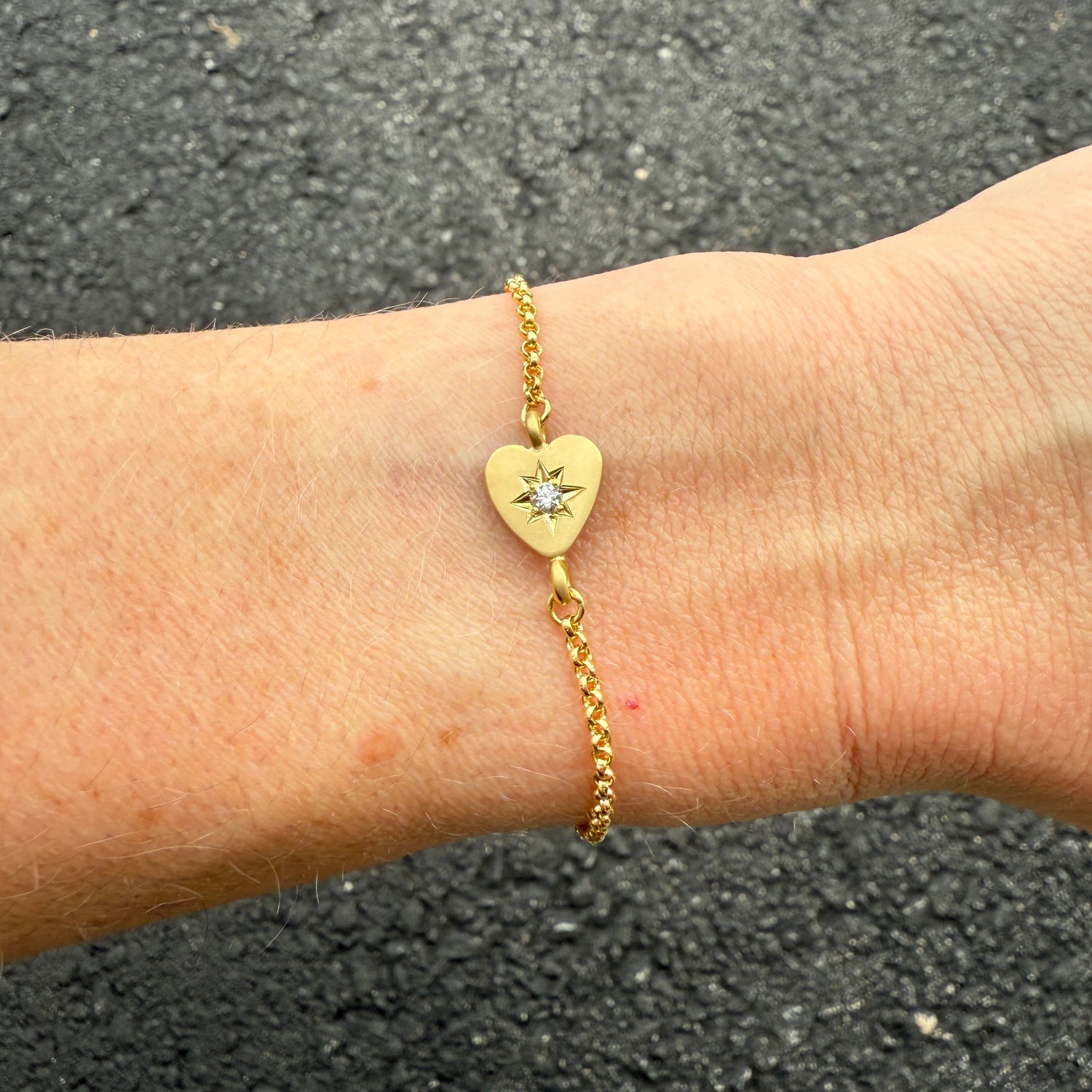 Detailed shot of the bracelet's lobster clasp and the "18k" stamp on the back of the heart charm, emphasizing craftsmanship.