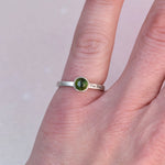 Green tourmaline bezel ring worn on a hand, showing the engraved phrase “One Day At A Time” on the silver band.