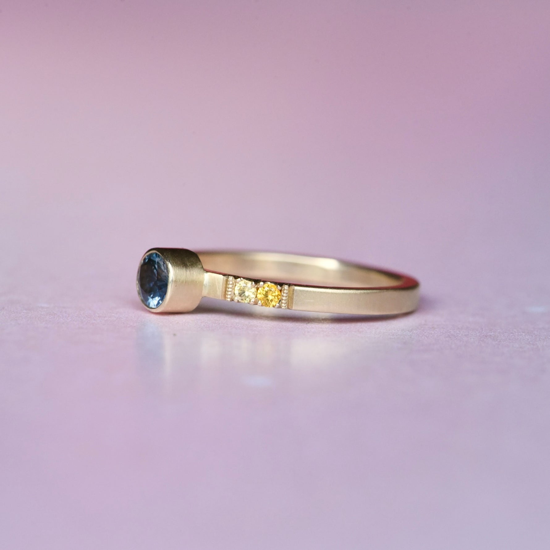Side profile of handcrafted Montana sapphire ring in 10k gold, showcasing the gradient of orange to deep pink sapphires with intricate milgrain and durable gold band.