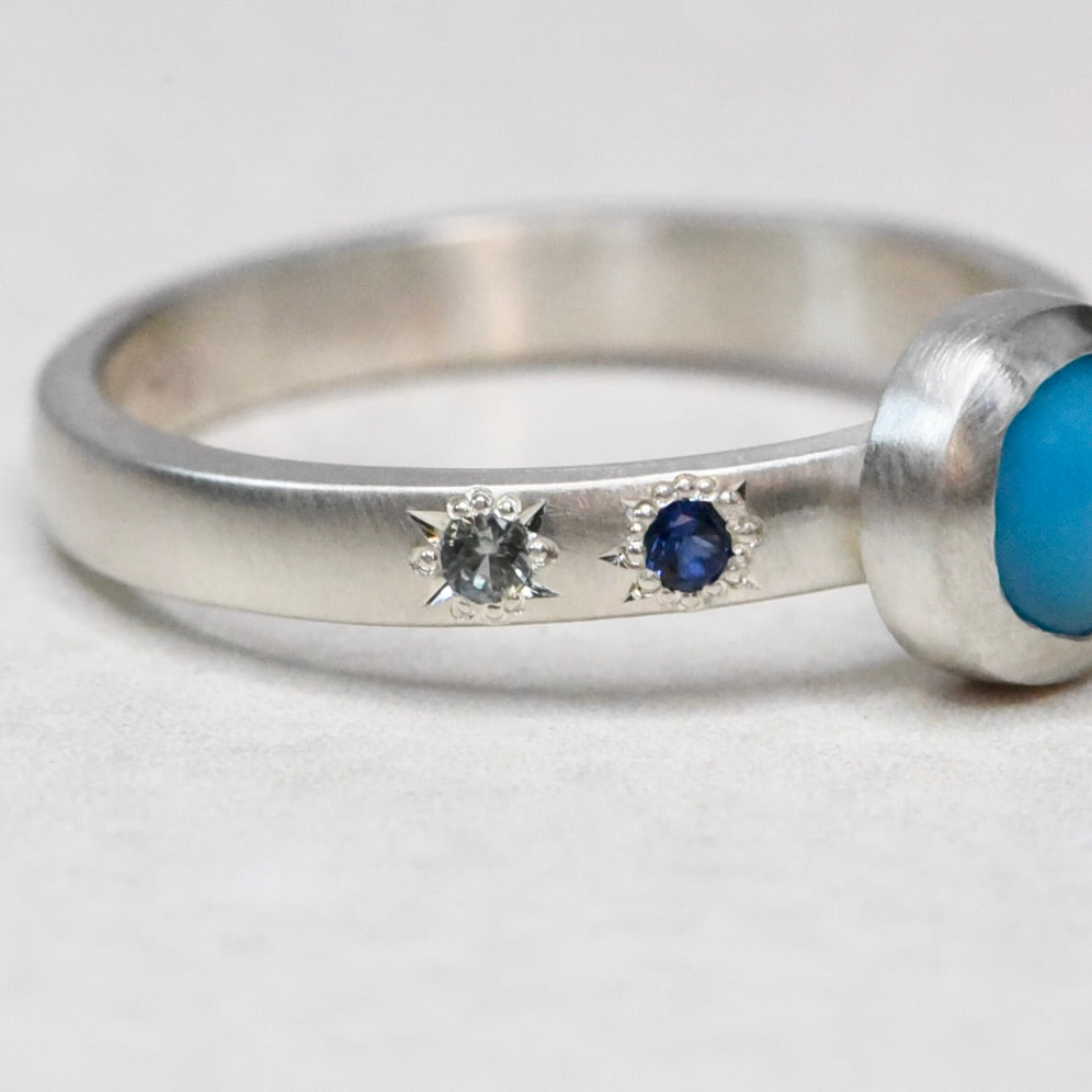 Close-up of the bezel-set Sleeping Beauty turquoise and sapphire star engravings on a handmade sterling silver band by Corkie Bolton Jewelry.