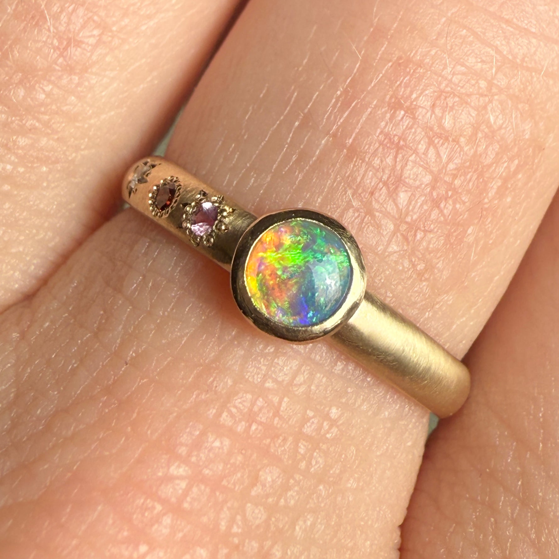 Close-up of the Lightning Ridge black opal cut by Ancients17, showing vivid flashes of green, blue, and neon orange in a smooth bezel setting on a handcrafted 14k yellow gold band.