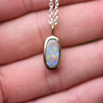 Hand holding a Lightning Ridge crystal opal pendant bezel set in 22k yellow gold showing red orange blue and green play of color