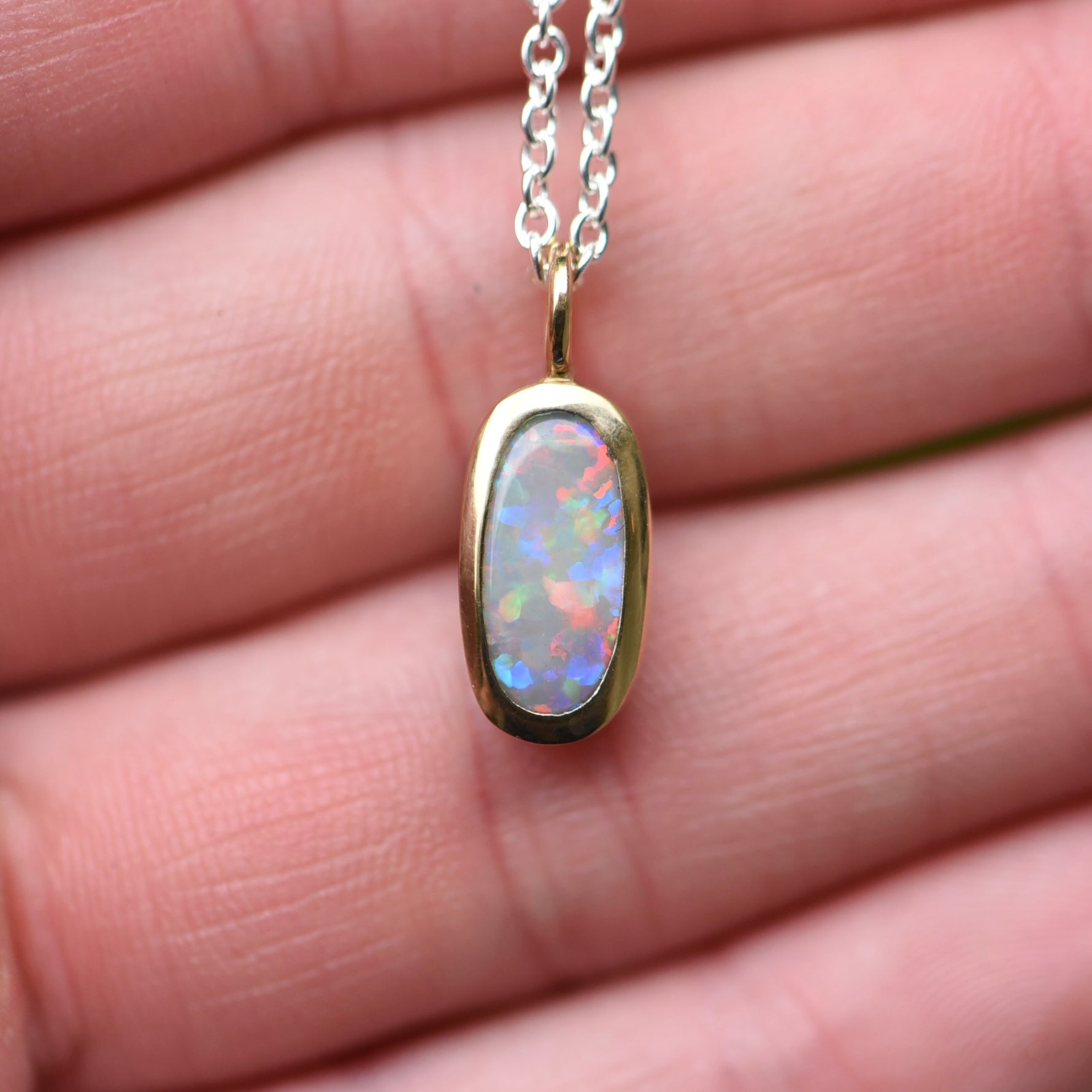 Hand holding a Lightning Ridge crystal opal pendant bezel set in 22k yellow gold showing red orange blue and green play of color