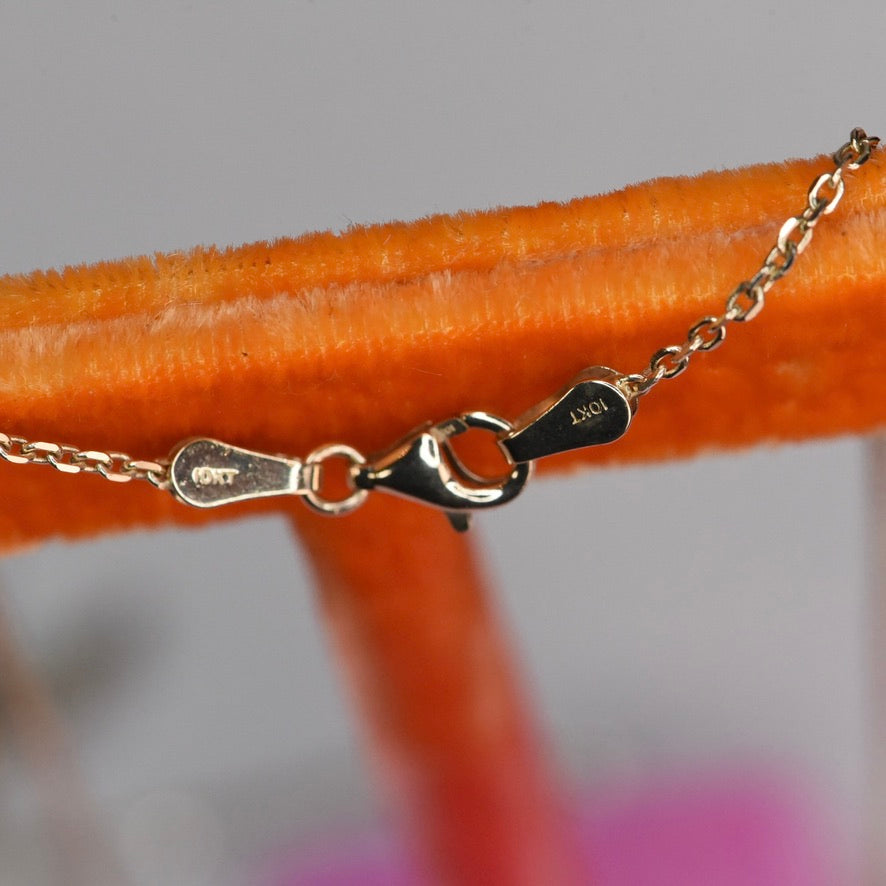Close-up of a gold chain with clasp on an orange surface
